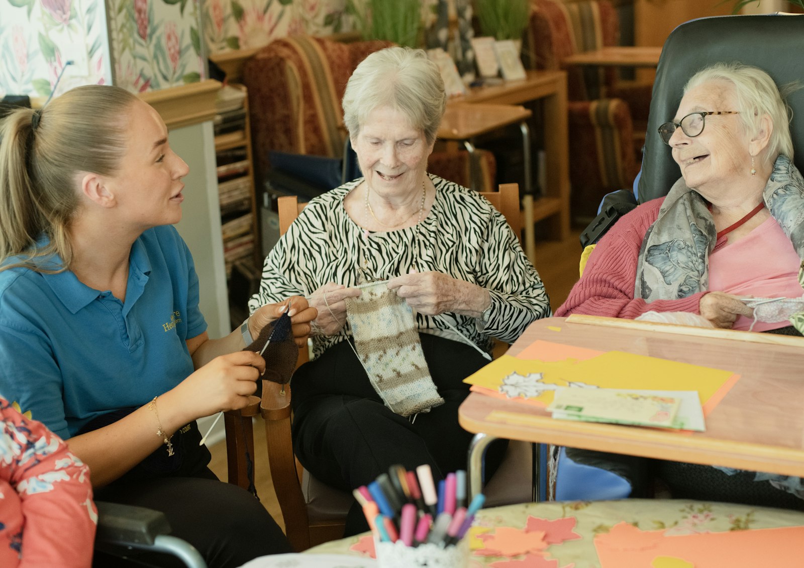A care worker sits with two residents in a care home lounge